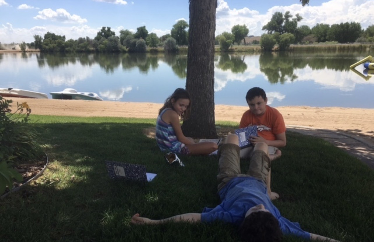 Three children relaxing under tree by lake